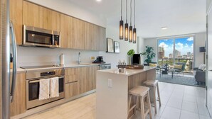 A modern kitchen with wooden cabinets, stainless steel appliances, and a central island with stools. - One Bedroom Condo King Bed With City Views (Miami)