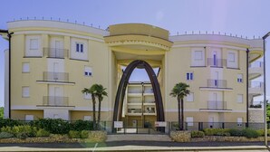 A multi-story hotel with a central archway entrance, balconies on each floor, and a stone facade. - ADRIA house with apartments / Adria APARTMENT C3 (Umag)