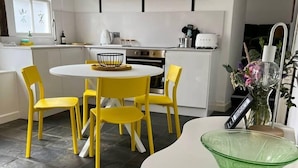 A modern kitchen with white cabinets, a round dining table with yellow chairs, and a green glass bowl on a white countertop. - 2 Bed Grade 2 - Dates Back to 1500's (Colchester)