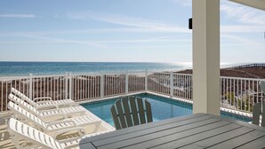 Uma área de piscina com cadeiras de descanso brancas e uma mesa, com vista para o oceano.