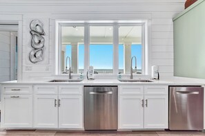 Une cuisine moderne avec des meubles blancs, des appareils en acier inoxydable et une grande fenêtre donnant sur un balcon.