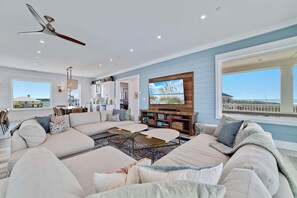 A spacious living room with a large sectional sofa, a coffee table, and a television mounted on a wooden wall.