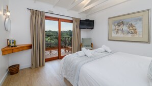 Een slaapkamer met een bed, een televisie, een schilderij, een raam met gordijnen en een balkon.