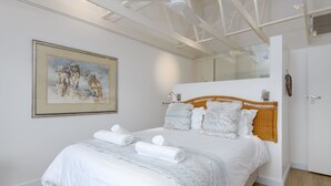 Een moderne slaapkamer met een groot bed, een schilderij aan de muur en een badkamers deur.