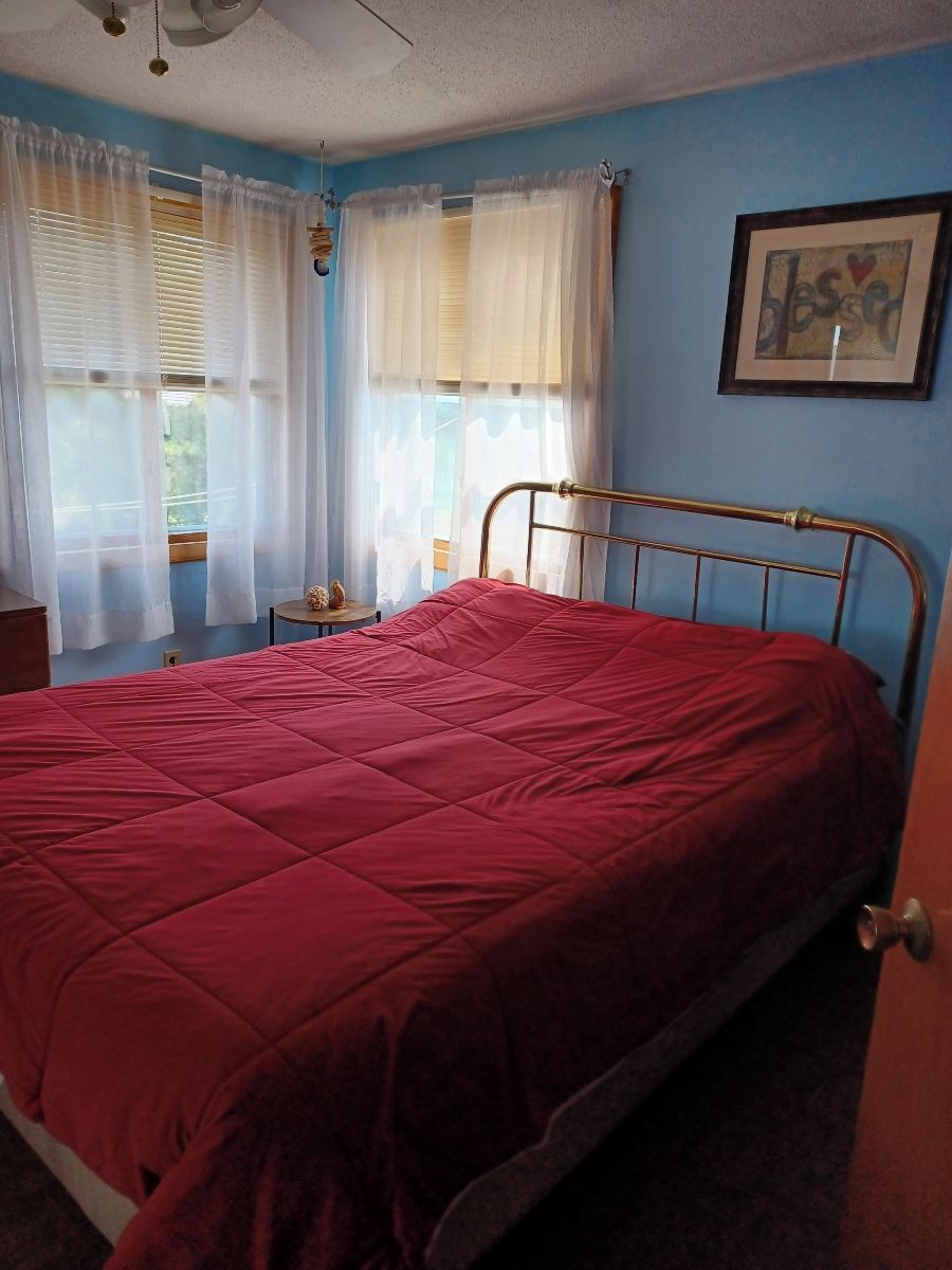 Une chambre à coucher avec un lit en métal, une couvre-lit rouge et des rideaux blancs.