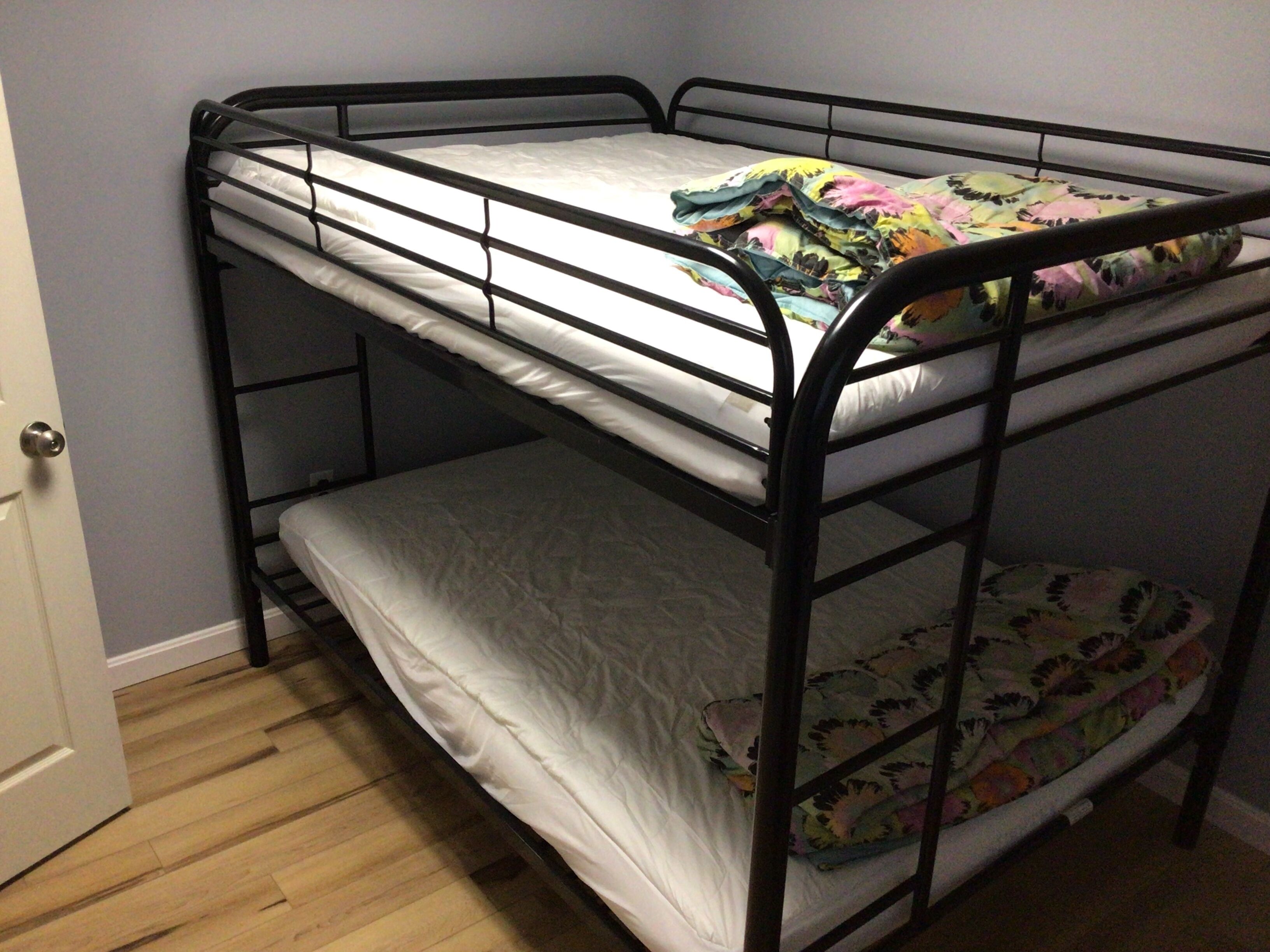 A bunk bed with a floral bedspread and a plain white mattress on the top bunk.