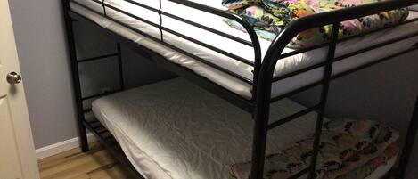 A bunk bed with a floral bedspread and a plain white mattress on the top bunk.