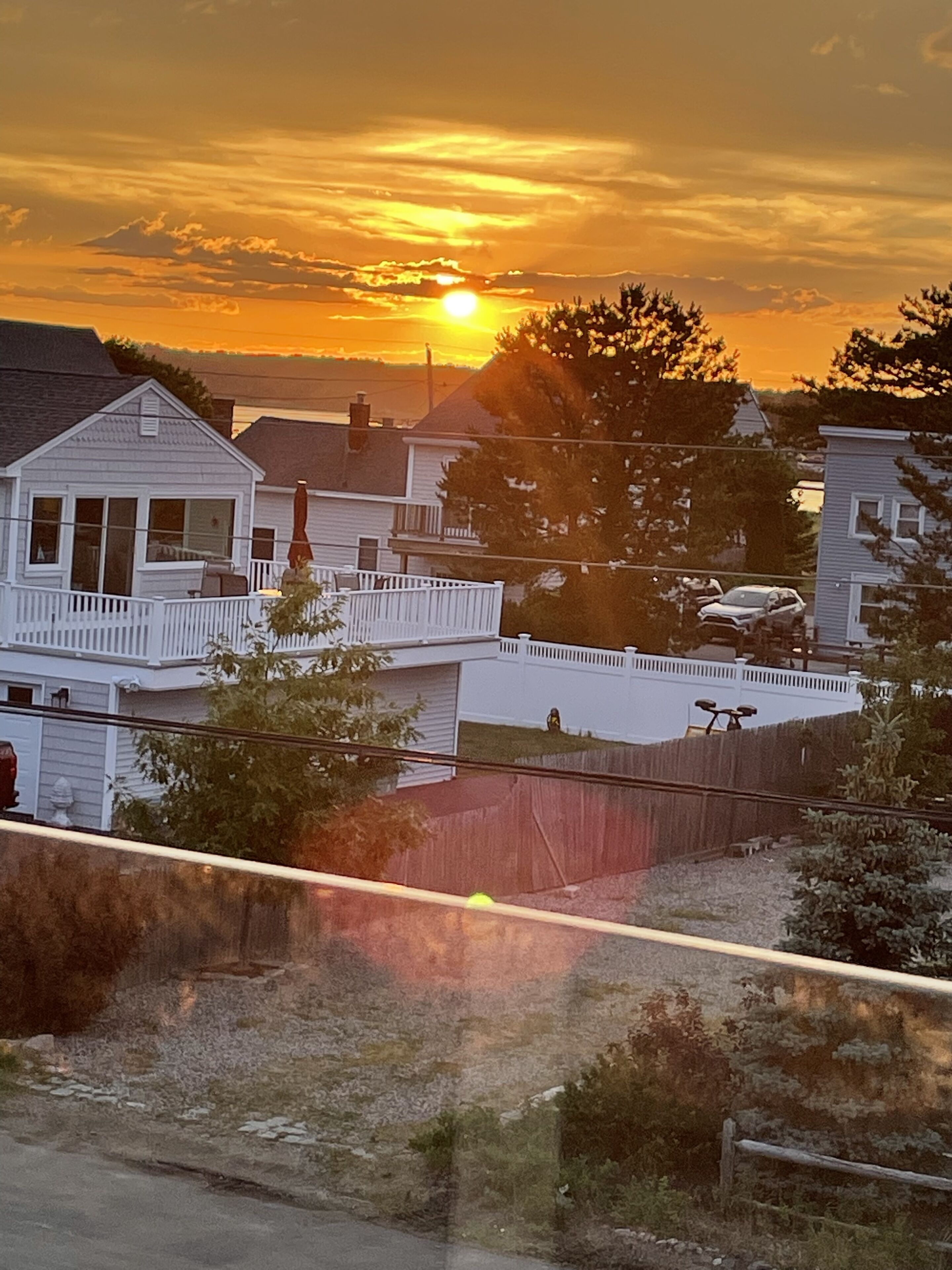 Un quartier résidentiel avec des maisons, une clôture en bois et un ciel dégagé au coucher du soleil.