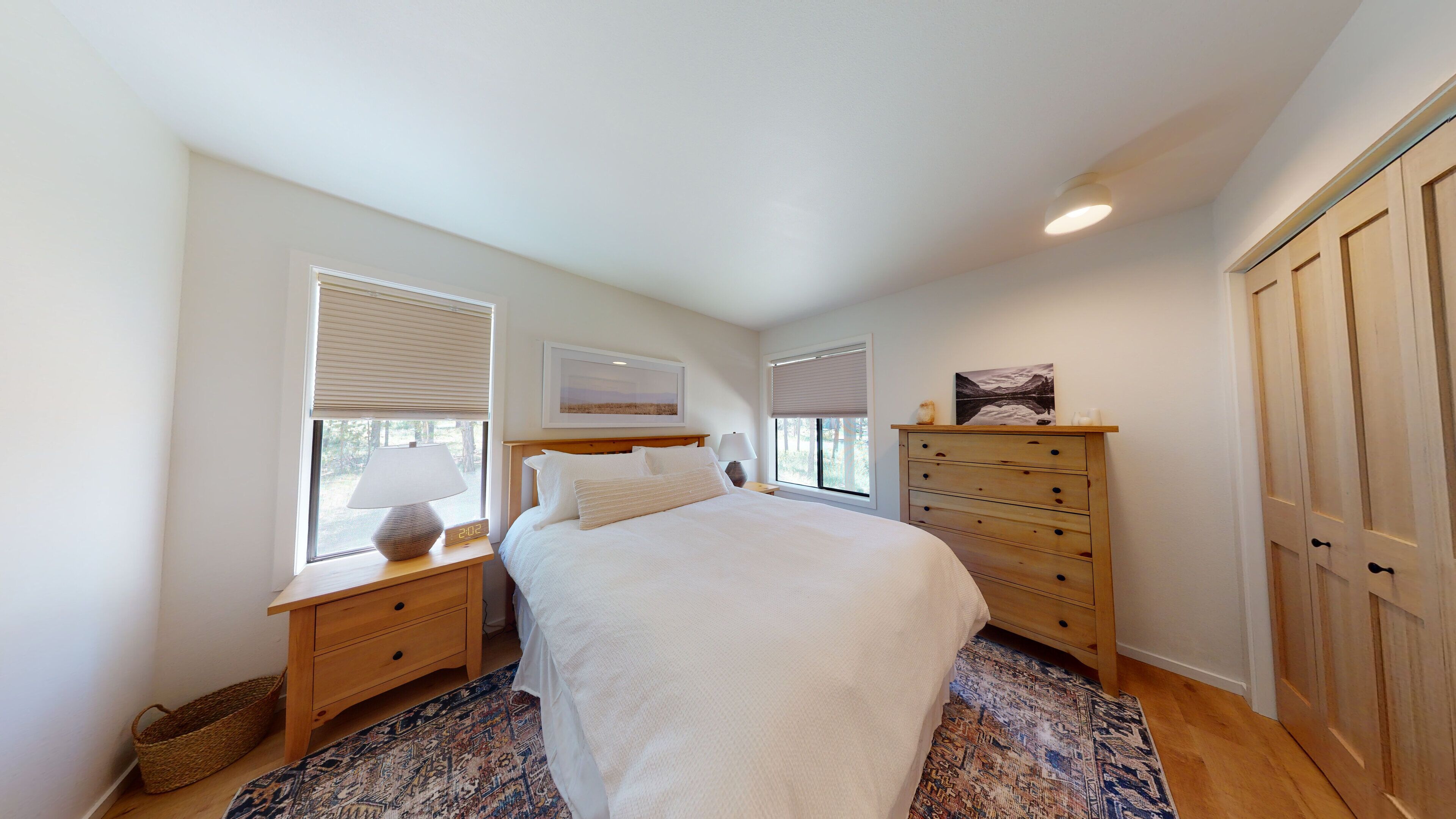 A bedroom with a bed, wooden nightstands, a dresser, and a large window with blinds.