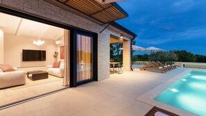A modern house with a swimming pool, a dining area, and a living room with a TV.