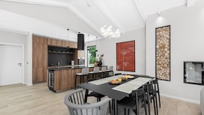 Eine moderne Küche mit Holzausstattung, einer zentralen Kochinsel und einem Essbereich mit schwarzem Tisch und Stühlen.