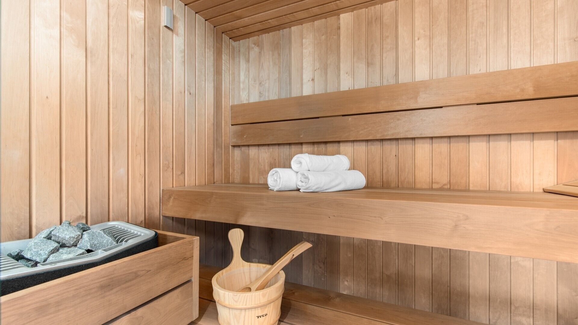 Uma sala de sauna de madeira com bancos, sauna e um balde de madeira com concha.