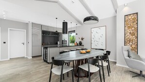 Una cocina moderna con una isla central, lámparas colgantes negras y un comedor con mesa y sillas redondas.