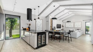 Una cocina moderna con una isla central, zona de comedor con sillas, un sofá y un televisor.