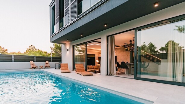 Een modern huis met een zwembad, buitenmeubilair en een glazen deur naar de binnenruimte.