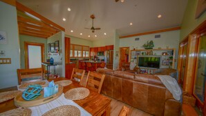 A spacious living room with a brown leather sofa, wooden dining table with placemats, and a television in the background. - Captivating Cabana – Luxury home, Boat Slip, Golf Cart, Pool, Pickleball, & Club (North Captiva)