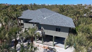 A two-story house with a grey roof, surrounded by palm trees and other vegetation. - Captivating Cabana – Luxury home, Boat Slip, Golf Cart, Pool, Pickleball, & Club (North Captiva)