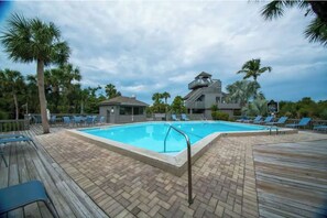 Une piscine avec des chaises longues, une terrasse en bois et un bâtiment avec une tour en arrière-plan.