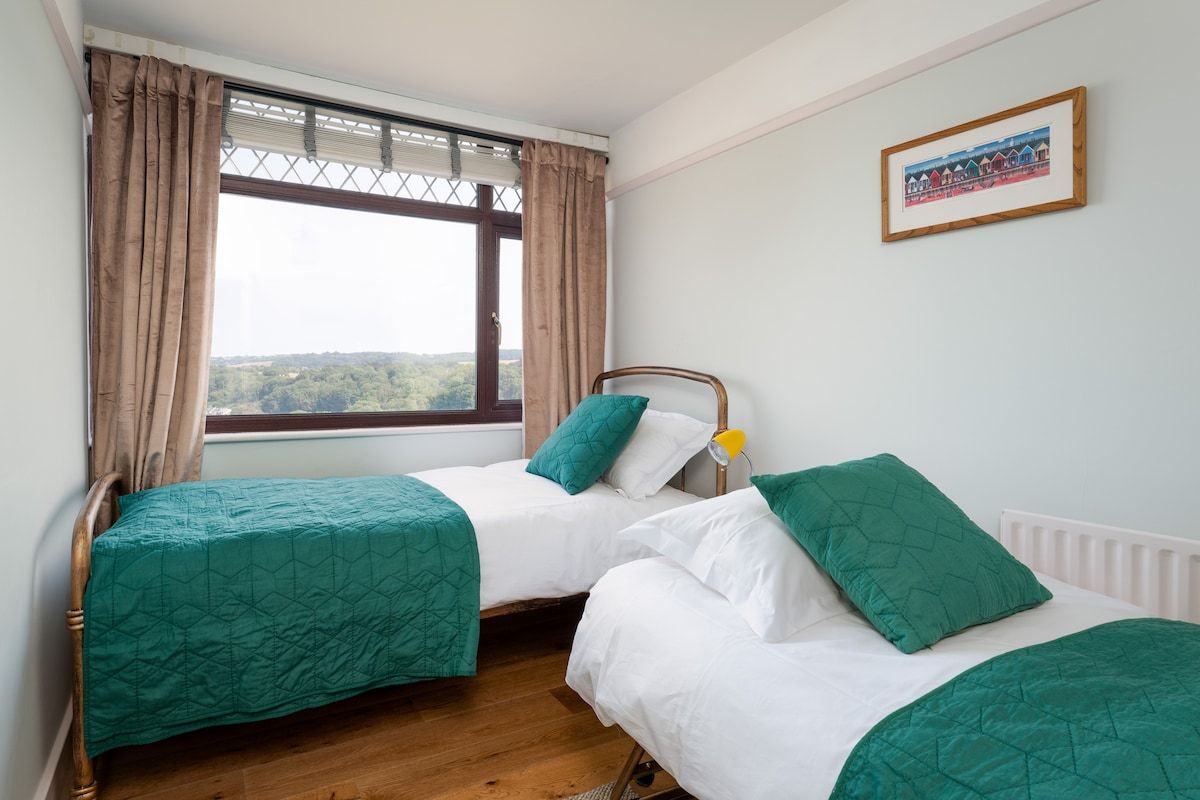 A room with two beds, a window with curtains, a radiator, and a framed picture on the wall.