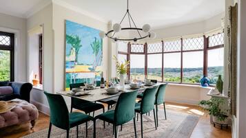 A dining area with a view, featuring a table set for six, green chairs, and a large painting on the wall.