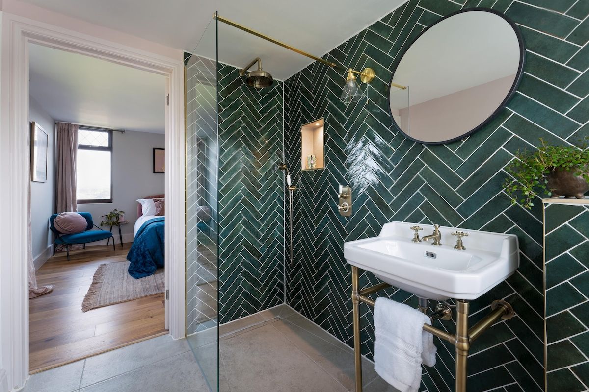A modern bathroom with a herringbone tile pattern, a white sink with gold fixtures, and a glass-enclosed shower.