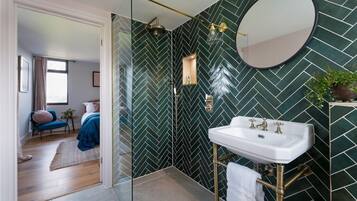 A modern bathroom with a herringbone tile pattern, a white sink with gold fixtures, and a glass-enclosed shower.