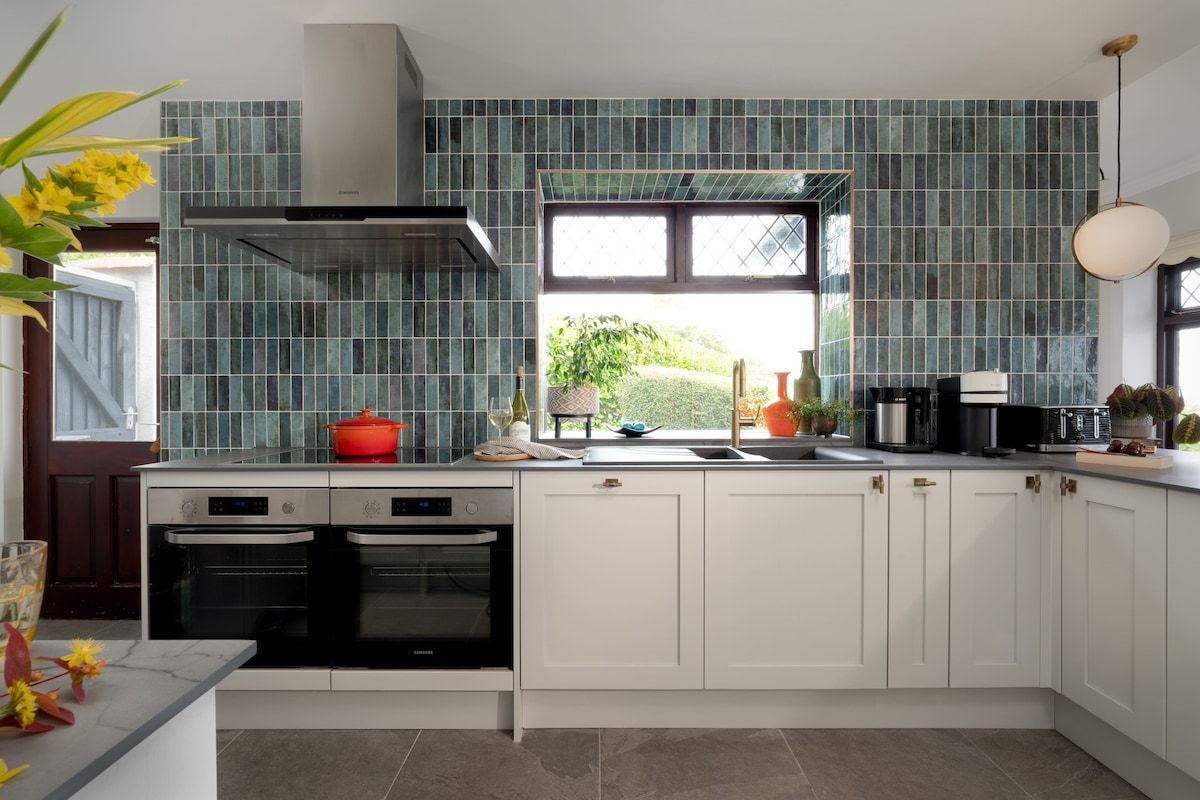 A modern kitchen with white cabinets, a stainless steel range hood, and a window with a view of greenery.