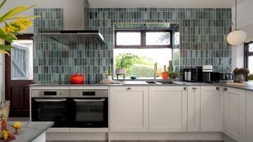A modern kitchen with white cabinets, a stainless steel range hood, and a window with a view of greenery.