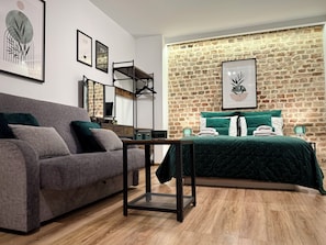 A modern bedroom with a brick wall, a grey sofa, a bed with green bedding, and artwork on the walls. - Prosta Butelkowa (Torun)