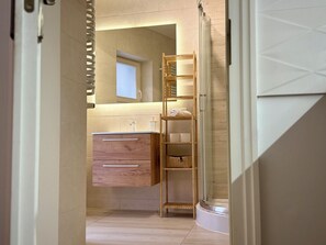 A bathroom with a wooden vanity, a shelf with towels, and a glass shower enclosure. - Prosta Butelkowa (Torun)