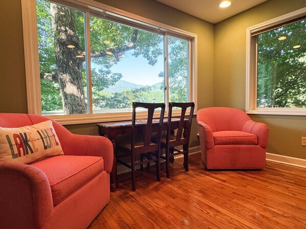 Une pièce avec un plancher en bois, une table à manger avec des chaises, un canapé rouge et une fenêtre donnant sur des arbres.