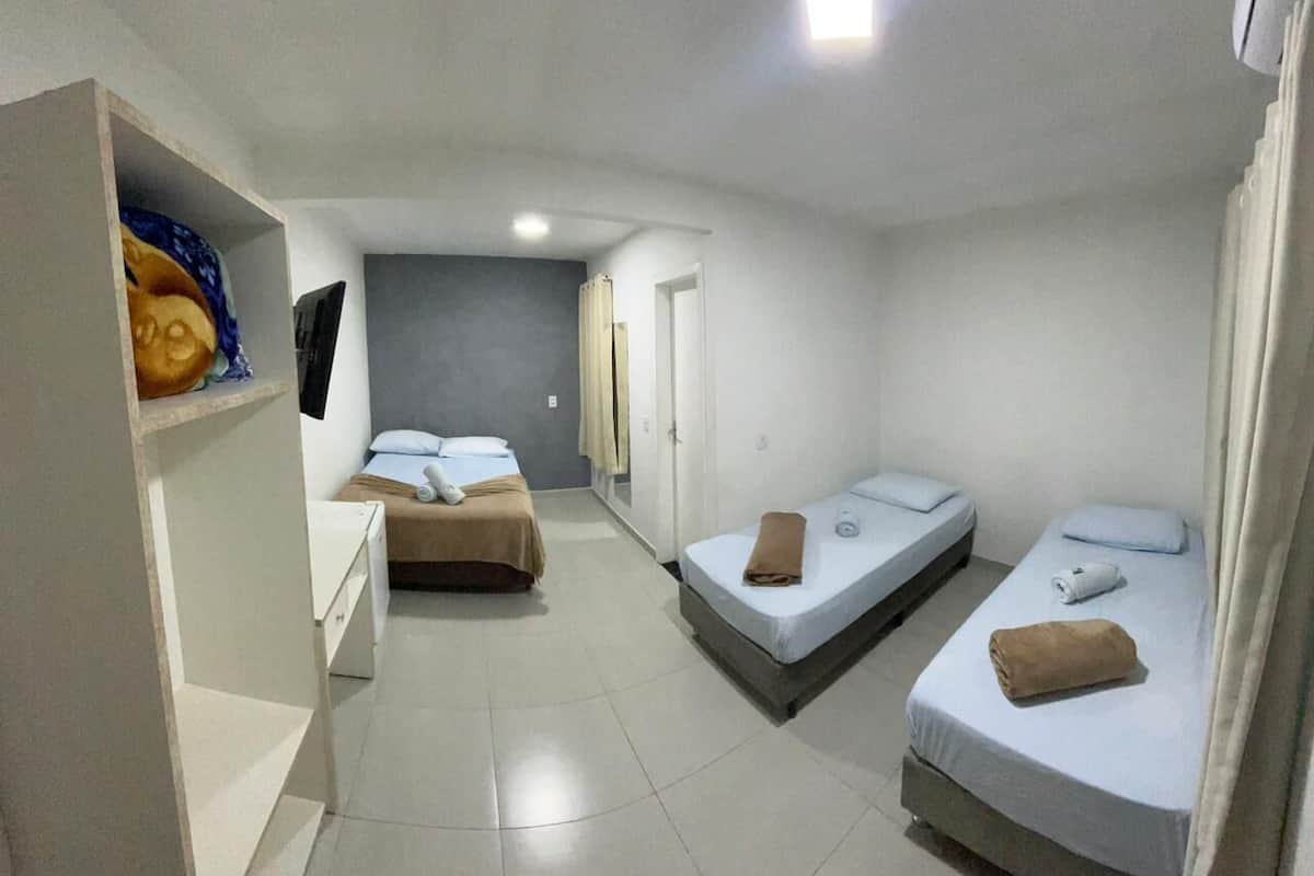 Quarto pequeno e limpo, com duas camas de solteiro, um guarda-roupa branco e uma estante com um quadro.