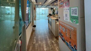 A hotel corridor with a tiled floor, a reception desk with a Christmas tree, and a poster advertising a TripAdvisor program. - Pousada Graff (Penha)