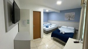 A hotel room with a bed, a desk, a TV, and a door leading to another room. - Pousada Graff (Penha)