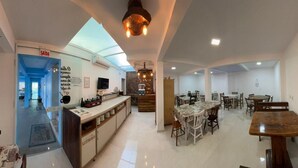 A spacious kitchen with a central island, a dining area with multiple tables, and a bright interior with natural light. - Pousada Graff (Penha)