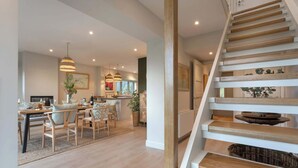 A modern kitchen with wooden flooring, a dining area with chairs and a table, and a staircase with wooden steps. - Barakat Lakes Escape | Ridgestone (Ambleside)