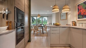 A modern kitchen with wooden cabinets, a built-in oven, and a dining area with a table and chairs. - Barakat Lakes Escape | Ridgestone (Ambleside)