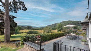 A patio with a table and chairs, a stone wall, and a view of a green landscape with hills. - Barakat Lakes Escape | Ridgestone (Ambleside)