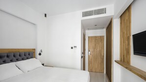 Un dormitorio con una cama grande, cabecera de madera, televisor montado en la pared y puerta que da a otra habitación.