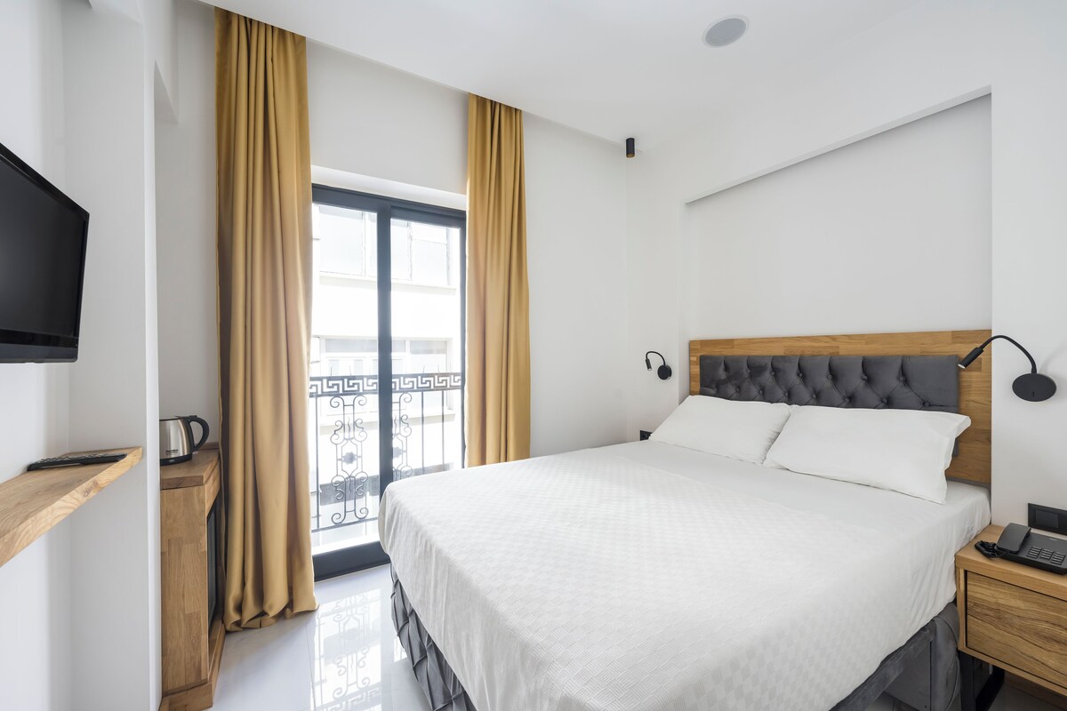 A hotel room with a bed, bedside table, TV, and a window with curtains.