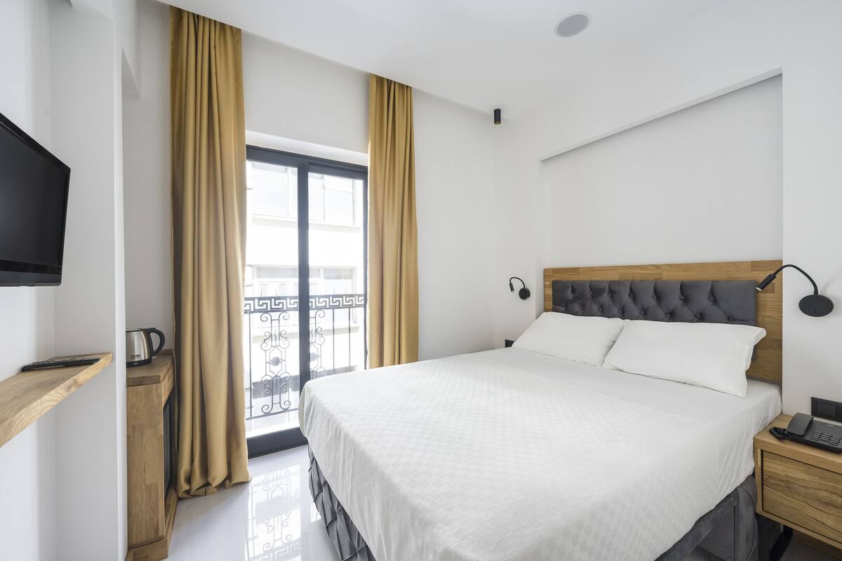 A hotel room with a bed, bedside table, TV, and a window with curtains.
