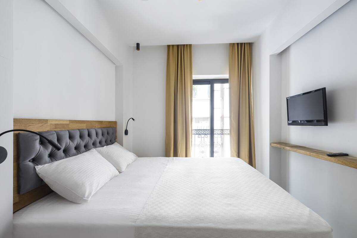 A modern hotel room with a large bed, a TV mounted on the wall, and a window with curtains.