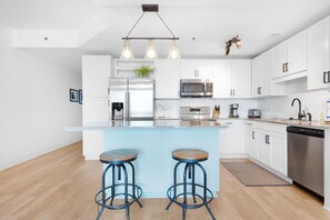 A modern kitchen with white cabinets, stainless steel appliances, a central island with stools, and pendant lighting. - GULF Views~Great Amenities~FIVE Pools~Walk to Beach~1BR Laketown Wharf 1714 (Panama City Beach)