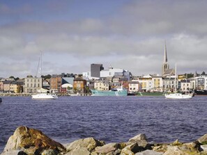 Eine Küstenstadtlandschaft mit historischen Gebäuden, einem Kirchturm und Booten auf dem Wasser.