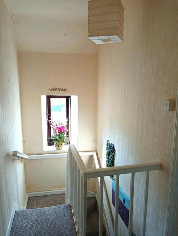 Eine enge Treppe mit einem 'Welcome'-Schild über einem Fenster voller Blumen.