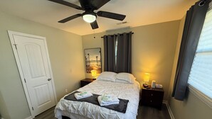 A neatly arranged bedroom with a bed, two bedside tables, a ceiling fan, and a window with curtains.