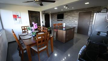 Une cuisine moderne avec un coin repas, comprenant un îlot central, des chaises en bois, un ventilateur de plafond et un four encastré.
