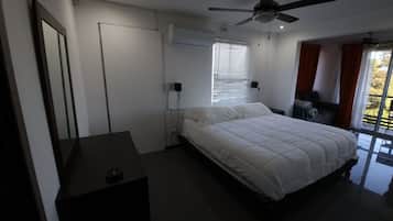 Une chambre à coucher avec un lit, un bureau, un ventilateur de plafond et une fenêtre avec des stores.