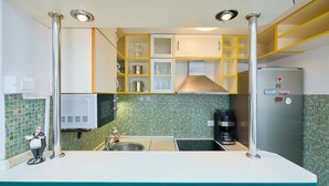 A compact kitchen with white countertops, a stainless steel sink, and a coffee maker. Yellow and white cabinets are above the counter, and a refrigerator is to the right. - Joyful Place (Dubrovnik)