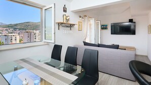 A modern living room with a glass dining table, black chairs, a grey sofa, and a TV mounted on the wall. - Joyful Place (Dubrovnik)